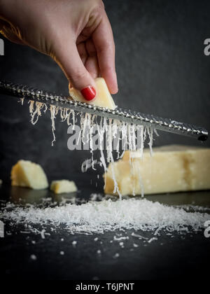 Hand einer Frau Gitter Parmesan auf schwarzem Hintergrund. Dunkle essen. Italienische Käse Parmigiano Reggiano Stockfoto