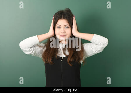 Lächelnd kleines Schulmädchen auf grünem Hintergrund. Junge verspielte Mädchen schließt Ihre Ohren Stockfoto