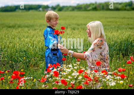 Mutter mit ihrem Sohn in einer herrlichen Wiese. Der junge überrascht ihre Mutter mit roter Mohn. Stockfoto