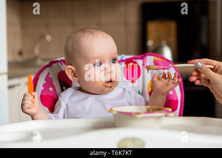 Baby ist 8 Monate und isst unabhängig. Der erste lure Baby. Das Baby mit blauen Augen nicht Gemüsebrei zu essen. mom Feeds von einem kleinen Kind' Stockfoto