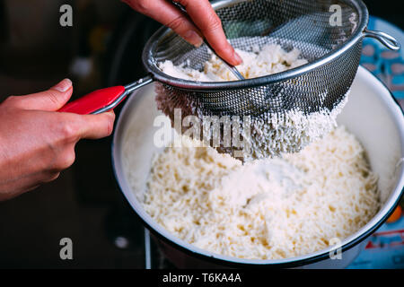 Der Prozess des Kochens hausgemachte Hüttenkäse. Hüttenkäse ist durch ein Sieb aus Molke gefiltert. Stockfoto