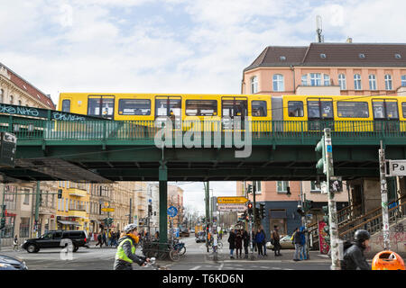 Fußgänger, Radfahrer und Verkehr an einer Kreuzung direkt neben dem Bahnhof Eberswalder Straße, während U-Bahn nähert sich der Bahnhof in Berlin Stockfoto