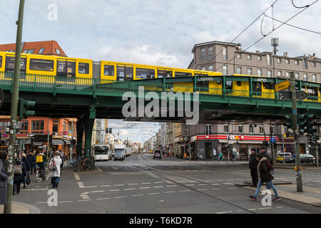 Fußgänger, Radfahrer und Verkehr an einer Kreuzung direkt neben dem Bahnhof Eberswalder Straße, während U-Bahn nähert sich der Bahnhof in Berlin Stockfoto