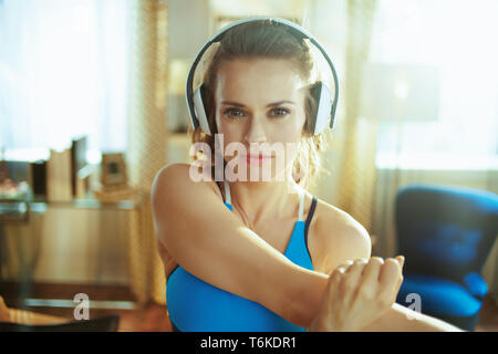 Portrait von gesunden Sport Frau in Fitness Kleidung Musik mit Kopfhörern und Stretching im modernen Haus. Stockfoto