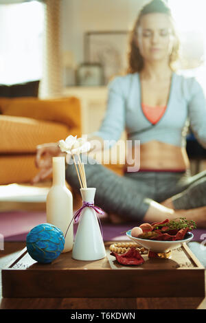 Nahaufnahme auf Fach mit duftenden Sachen für Aroma Yoga und passende Frau meditieren im Hintergrund in das moderne Haus. Stockfoto