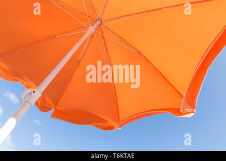 Ansicht von unten auf das orange Sonnenschirm vor blauem Himmel Stockfoto