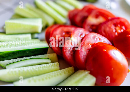 Frisch geschnittene reife rote Tomaten Scheiben auf Platte Tabelle als gesunder Snack oder Salat Vorspeise mit grünen Gurken Makro Nahaufnahme Stockfoto