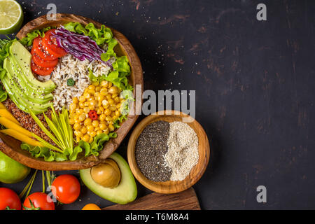 Buddha Schüssel mit Kichererbsen, Avocado, wilder Reis, Quinoa Samen, Paprika, Tomaten, grüne, Kohl, Salat auf dunklen Tisch aus Stein und Holz- Schüssel mit Stockfoto