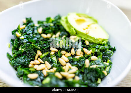 Makro Detailansicht von Kale green vegan vegetarisch Salat auf Holztisch mit Pinienkernen und Avocado Hälfte in der Schüssel Stockfoto