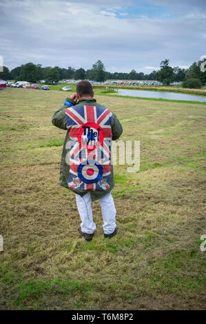 Scooter Enthusiast und Mod im Parka mit aufgenähtem Abzeichen für die Who und Union Jacks auf seinem Handy an der Stanford Hall, Leicestershire Stockfoto
