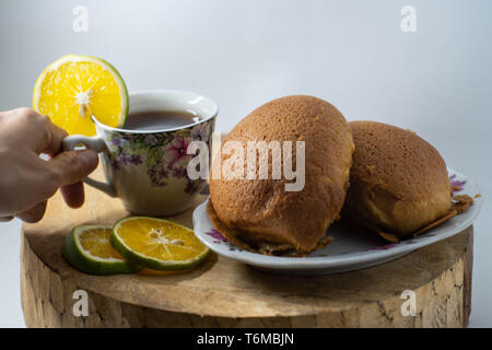 Zwei braune Brot auf den Teller und eine Tasse warmen Zitrone Tee sind auf einer hölzernen Matte, die mit einer isolierten weißen Hintergrund platziert Stockfoto