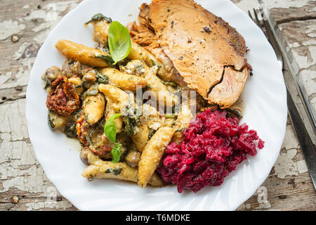 Schweinebraten mit Kartoffelklößen, Spinat, sonnengetrocknete Tomaten und Zucchini in Käsesoße mit Rote Bete Salat Stockfoto