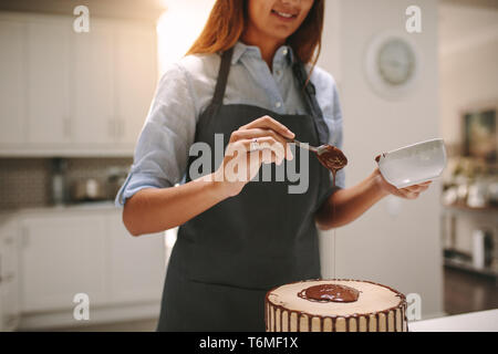 Frau giesst flüssige Schokolade auf dem Kuchen für die Verzierung. Köchin bereitet leckere Schokolade Kuchen in der Küche. Stockfoto