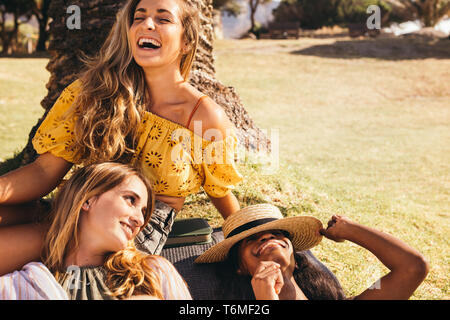 Drei fröhlichen Frauen sitzen in einem Park Spaß haben. Nahaufnahme von drei Frauen Freunde sitzen auf Gras in einem Park an einem sonnigen Tag lachend und entspannend. Stockfoto