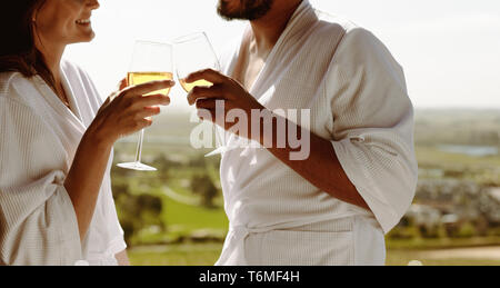 In der Nähe von ein paar toasten Weißwein. 7/8 Schuß von Mann und Frau im Bademantel im Gespräch bei einem Glas Wein. Stockfoto