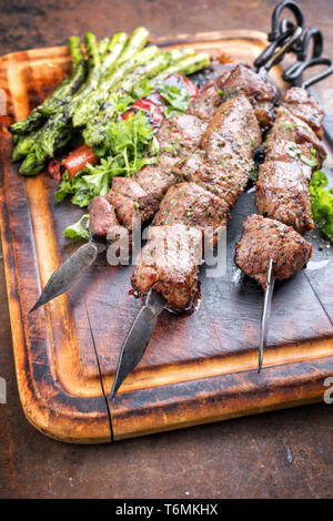 Traditionelle russische Schaschlik auf einem Grill Spieß mit grünem Spargel und Paprika aus nächster Nähe auf einer gebrannten Schneidebrett Stockfoto