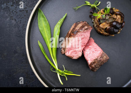 Traditionelle italienische Grill alter geschnittenes Rinderfilet mit Bärlauch und pioppinos als Draufsicht auf einem Teller mit Platz kopieren Stockfoto