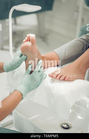 Qualifizierte Schönheit Master in Schutzhandschuhe reiben Beine von Ihrem Client Stockfoto