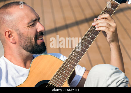 Porträt eines spanischen Mann mit Bart und kurzen buzz Haar, eine akustische Gitarre spielen im Freien. Stockfoto