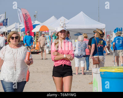 Eine junge Frau trägt ein rosafarbenes Hemd, schwarze Shorts und weißen Ball Cap sticht unter den Besuchern der 2019 Texas Sandfest in Port Aransas, Texas USA. Stockfoto