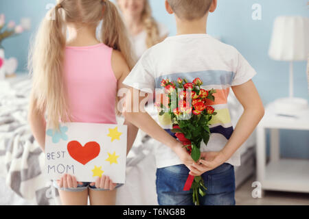 Kleine Kinder verstecken Geschenke für Mutter hinter ihrem Rücken zu Hause Stockfoto