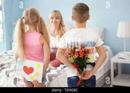 Kleine Kinder verstecken Geschenke für Mutter hinter ihrem Rücken zu Hause Stockfoto