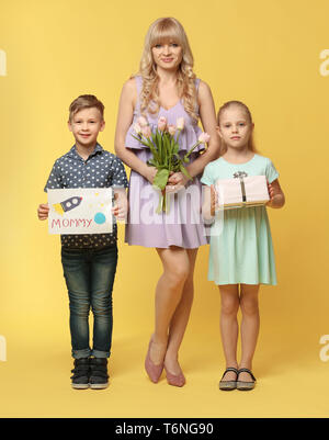 Portrait von niedlichen kleinen Kinder und ihre Mutter mit Geschenken auf farbigen Hintergrund Stockfoto