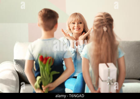 Kleine Kinder verstecken Geschenke für Mutter hinter ihrem Rücken zu Hause Stockfoto