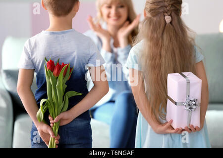 Kleine Kinder verstecken Geschenke für Mutter hinter ihrem Rücken zu Hause Stockfoto