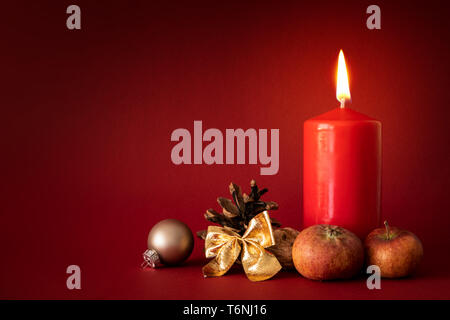 Weihnachtsdekoration mit einer brennenden Kerze auf rotem Hintergrund Stockfoto