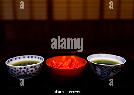 Traditionelle japanische Schalen Tassen mit Matcha grüner Tee und Erdbeeren in machiya Haus mit Schwarz lackiertem Holz Tisch und Nachtisch Stockfoto