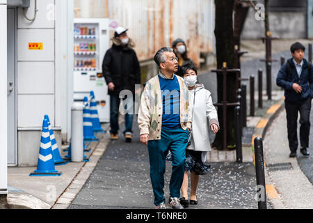 Tokyo, Japan - 31. März 2019: Ginza oder Akasaka Bezirk mit Menschen Touristen senior Paar zu Fuß auf der Straße Straße Straße und gefallenen Cherry Blossom Stockfoto