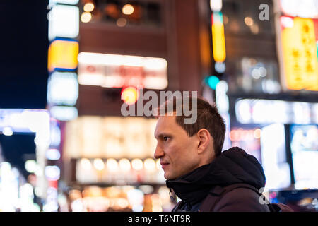 Tokio, Japan Bezirk Shinjuku bei Nacht mit jungen Mann Seite Profil Portrait auf Nachtleben mit Hintergrund bokeh Lichter auf der Straße Stockfoto