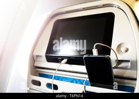 Passagier auf einer Ebene mit dem Ladegerät für Smart Phone während des Fluges. Ladestation auf Ebene. Stockfoto