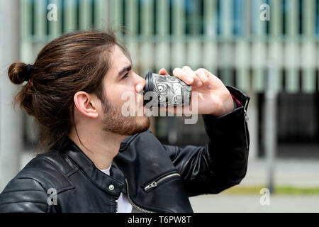 Porträt einer stattlichen modischer hipster Mann in einem schwarzen Lederjacke Trinken von Tee oder Kaffee aus einem schwarzen Takeaway Pappbecher außerhalb. Stockfoto