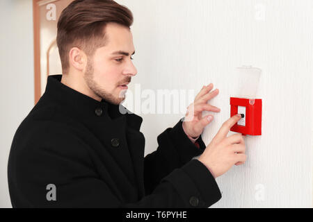 Junger Mann drücken der Taste der Brandmeldeanlage, innen Stockfoto