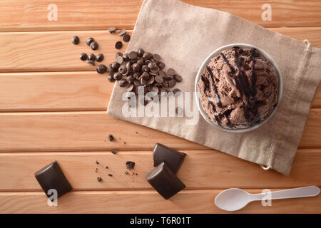 Choco Eisbecher mit Chips und Waffel auf Stoff sack auf einen hölzernen Tisch eingerichtet. Horizontale Komposition. Ansicht von oben. Stockfoto