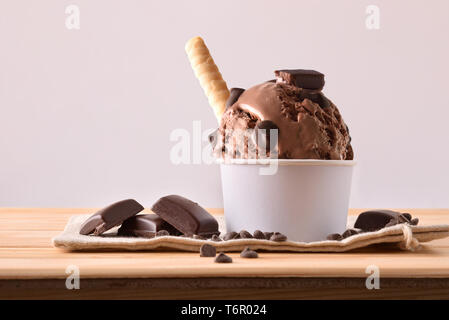 Choco Eisbecher mit Chips und Waffel auf Stoff sack auf einen hölzernen Tisch eingerichtet. Horizontale Komposition. Vorderansicht. Stockfoto