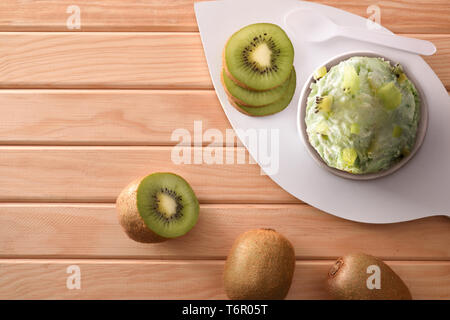 Kiwi Eisbecher mit Stücken und Scheiben von Kiwis auf einem hölzernen Tisch eingerichtet. Horizontale Komposition. Ansicht von oben. Stockfoto