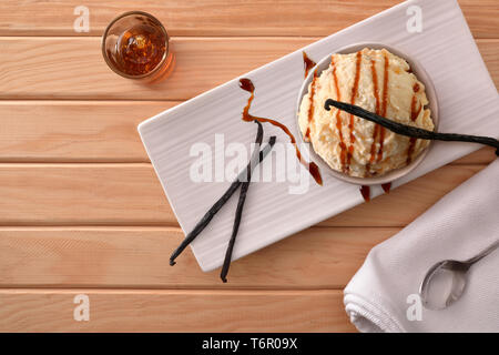 Vanille und Karamell Eis mit Vanilleschoten auf einem Schild an einem hölzernen Tisch eingerichtet. Horizontale Komposition. Ansicht von oben. Stockfoto