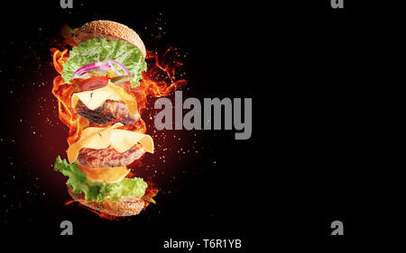 Eine feurige fliegende doppelten Cheeseburger auf schwarzem Hintergrund. Stockfoto