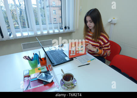 In einem Klassenzimmer. Lehrerin vor dem Laptop sitzen und lesen Englisch Buch. Kiew, Ukraine. November 28, 2018 Stockfoto