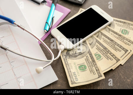 Geld mit Telefon und Stethoskop auf Tisch Stockfoto