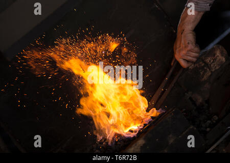 Nahaufnahme der Hand des männlichen Nagel Maker bei Workshop Feuerstelle mit Vintage schmied Zangen heißes Metall in wütende Feuer zu halten, Black Country Living Museum, Großbritannien. Stockfoto