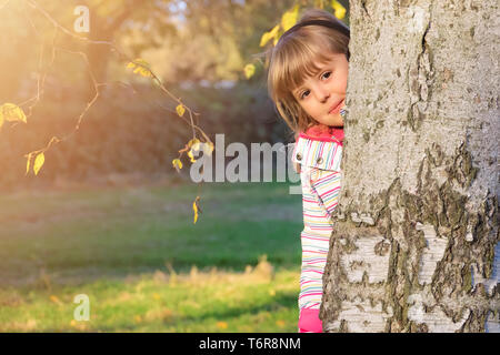 Süße kleine Mädchen versteckt sich hinter einem Baum Stockfoto