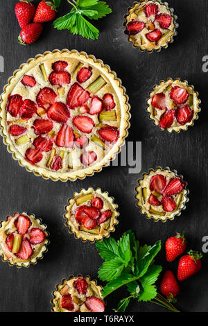 Hausgemachte Kuchen mit Erdbeeren und Rhabarber auf schwarzem Holz- Hintergrund. Ansicht von oben. Im rustikalen Stil Stockfoto