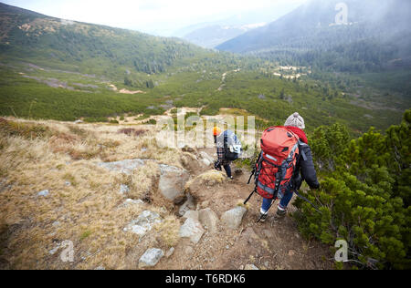 Jungen Touristen wandern in der Gruppe gemeinsam auf schöne natürliche Straße in grüne Wiese und schönen großen Bergen umgeben. Stockfoto