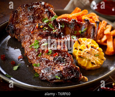 Scharf marinierte gegrillte Portion Spare Ribs mit gegrillten Maiskolben auf einem Schild in der Nähe zu sehen, für Werbung serviert. Stockfoto