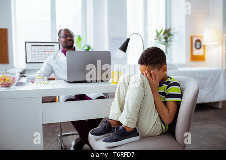 Sohn spielen Tricks beim Besuchen der Vater Arbeiten am Laptop Stockfoto