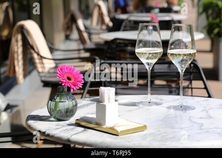 Tabelle in einer Straße, Restaurant, romantisches Essen, elegante Kulisse für Feier und Datum. Zwei Gläser Champagner, Servietten und Blüten auf einem Tisch Stockfoto